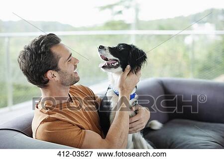 Stock Photo - Smiling man petting dog on sofa. Fotosearch