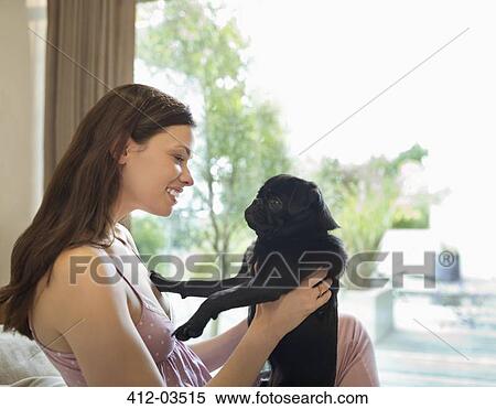 Stock Photography - Smiling woman holding dog on bed. Fotosearch