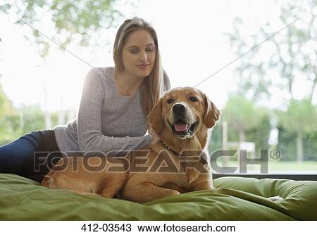 Stock Image - Woman petting dog on bed. Fotosearch