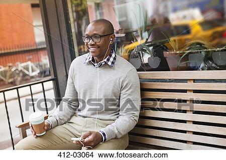 Picture - Man listening to earphones on city street. Fotosearch