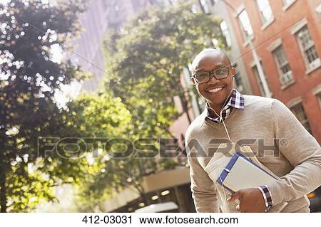 Stock Image - Man listening to earphones on city street. Fotosearch