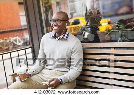 Man listening to earphones on city street View Large Photo Image Stock Image - Man listening to earphones on city street. Fotosearch