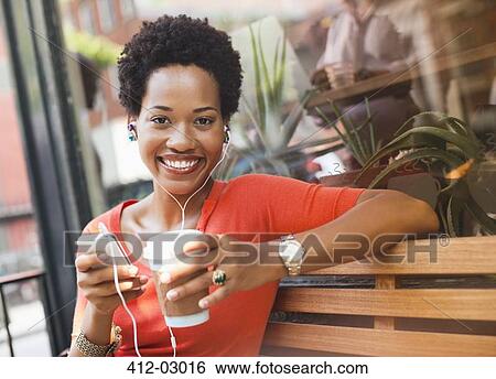 Stock Photograph - Woman listening to earphones by coffee shop. Fotosearch
