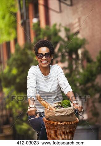 Woman riding bicycle on city street View Large Photo Image Stock Image - Woman riding bicycle on city street. Fotosearch
