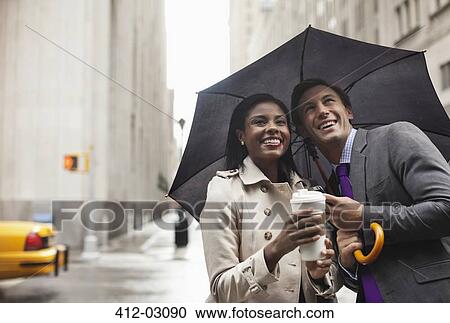 Stock Image - Business people holding umbrella on city street. Fotosearch