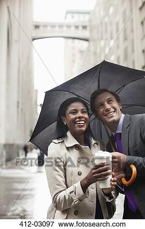 Stock Photo - Business people holding umbrella on city street. Fotosearch