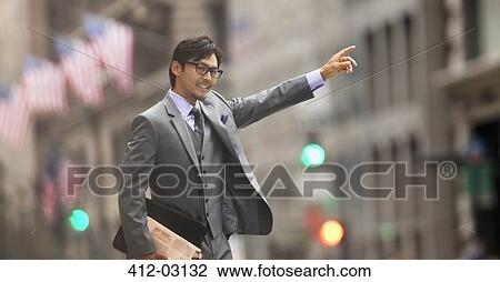 Stock Image - Businessman hailing taxi on city street. Fotosearch