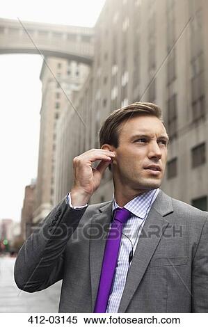 Businessman listening to earphones on city street View Large Photo Image Stock Photography - Businessman listening to earphones on city street. Fotosearch