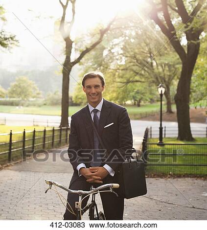 Stock Image - Businessman sitting on bicycle in urban park. Fotosearch