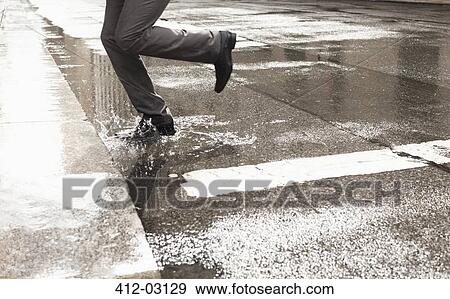 Businessman stepping in puddle on city street View Large Photo Image Stock Photo - Businessman stepping in puddle on city street. Fotosearch