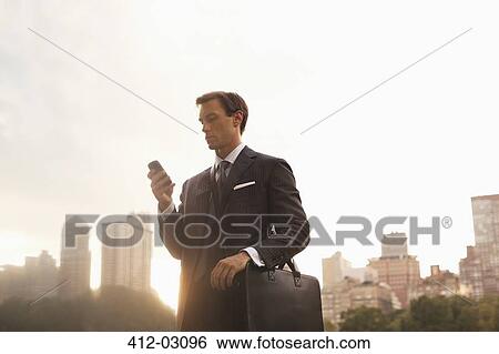 Stock Photograph - Businessman using cell phone in urban park. Fotosearch
