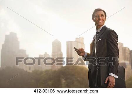 Businessman using cell phone in urban park View Large Photo Image Stock Photograph - Businessman using cell phone in urban park. Fotosearch