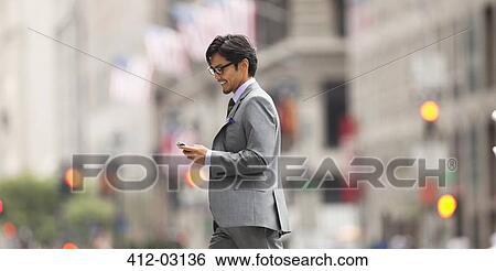 Stock Photograph - Businessman using cell phone on city street. Fotosearch
