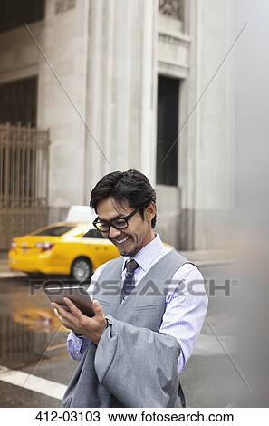 Stock Image - Businessman using tablet computer on city street. Fotosearch