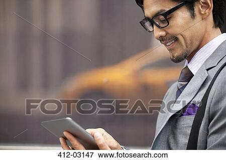 Stock Photo - Businessman using tablet computer on city street. Fotosearch