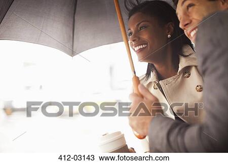 Stock Image - Businesspeople huddled under umbrella. Fotosearch