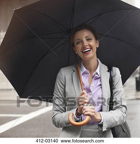 Stock Image - Businesswoman holding umbrella on city street. Fotosearch