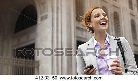 Stock Image - Businesswoman using cell phone on city street. Fotosearch