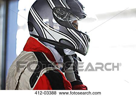 Stock Photo - Racer tying on helmet in garage. Fotosearch