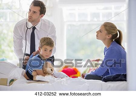 Stock Image - Doctor listening to boy's heartbeat at house call. Fotosearch