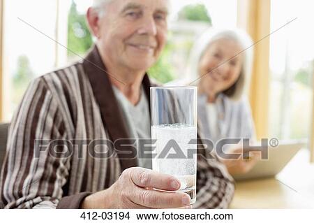 Picture - Older man taking medication in water. Fotosearch