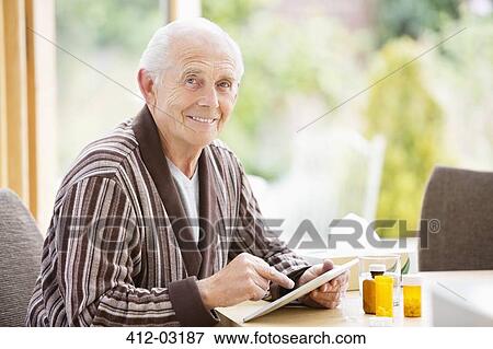 Stock Photo - Older man using tablet computer at table. Fotosearch