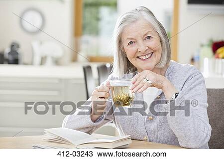 Stock Image - Older woman drinking tea and reading. Fotosearch