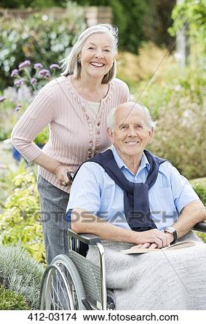 Picture - Older woman pushing husband's wheelchair outdoors. Fotosearch
