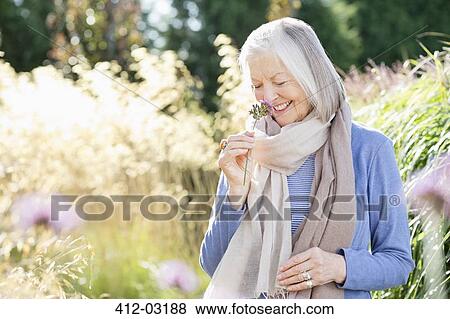 Stock Photo - Older woman smelling flowers outdoors. Fotosearch