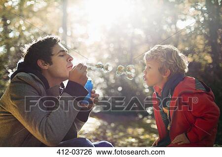 Father and son blowing bubbles in park View Large Photo Image Stock Photograph - Father and son blowing bubbles in park. Fotosearch