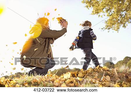 Stock Image - Father and son playing in autumn leaves. Fotosearch