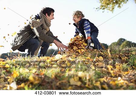 Stock Image - Father and son playing in autumn leaves. Fotosearch