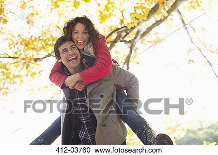 Man carrying girlfriend piggyback in park View Large Photo Image Stock Image - Man carrying girlfriend piggyback in park. Fotosearch
