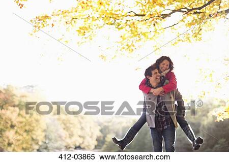 Stock Photography - Man carrying girlfriend piggyback in park. Fotosearch
