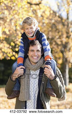Stock Image - Man carrying son on shoulders in park. Fotosearch