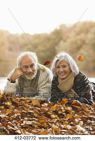 Stock Image - Older couple laying in autumn leaves. Fotosearch