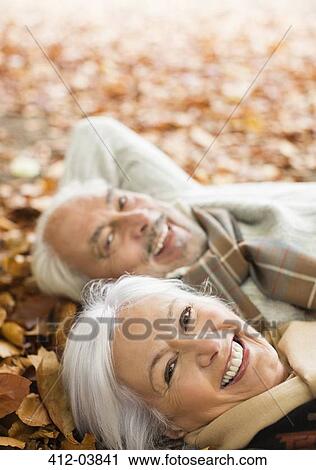Stock Image - Older couple laying in autumn leaves. Fotosearch