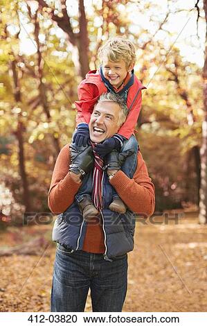 Stock Image - Older man carrying grandson on shoulders in park. Fotosearch