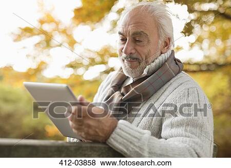 Older man using tablet computer in park View Large Photo Image Stock Photo - Older man using tablet computer in park. Fotosearch