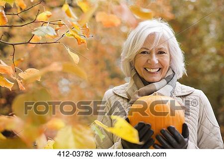 Older woman holding pumpkin in park View Large Photo Image Stock Image - Older woman holding pumpkin in park. Fotosearch