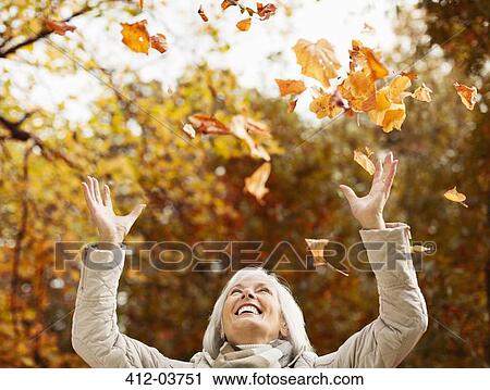 Older woman playing in autumn leaves View Large Photo Image Stock Image - Older woman playing in autumn leaves. Fotosearch