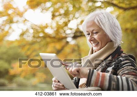 Older woman using tablet computer in park View Large Photo Image Stock Image - Older woman using tablet computer in park. Fotosearch