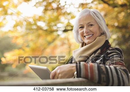 Stock Photo - Older woman using tablet computer outdoors. Fotosearch