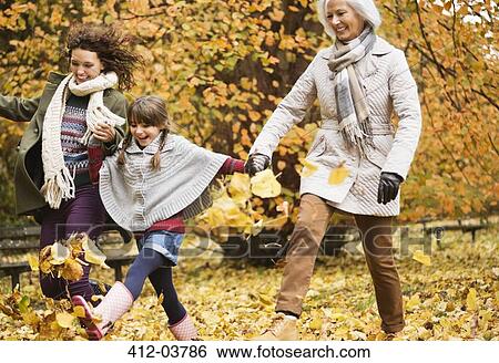 Stock Photograph - Three generations of women playing in autumn leaves. Fotosearch