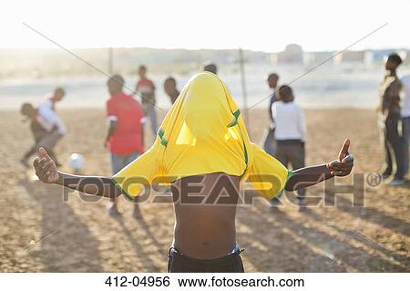 Boy celebrating with soccer jersey on his head in dirt field View Large Photo Image Stock Photograph - Boy celebrating with soccer jersey on his head in dirt field. Fotosearch