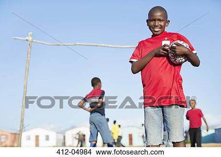 Picture - Boy holding soccer ball in dirt field. Fotosearch