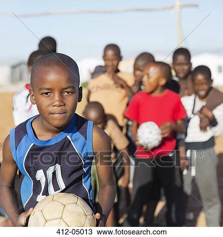 Stock Image - Boys holding soccer balls in dirt field. Fotosearch