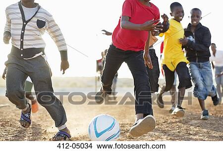 Picture - Boys playing soccer together in dirt field. Fotosearch