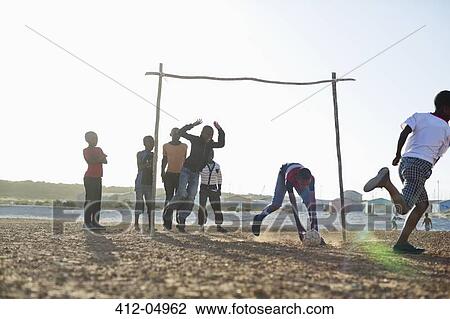 Stock Image - Boys playing soccer together in dirt field. Fotosearch