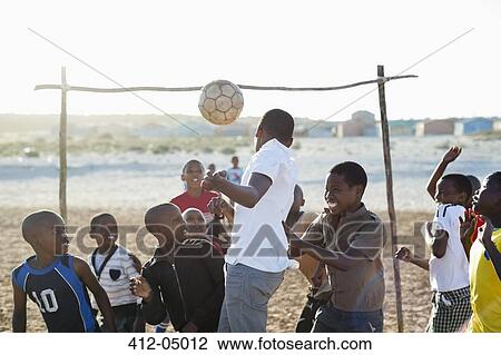 Stock Image - Boys playing soccer together in dirt field. Fotosearch